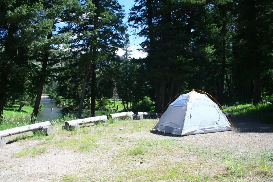 A light blue tent pitched at Slough Creek Campground Site #1 with trees and creek in the background