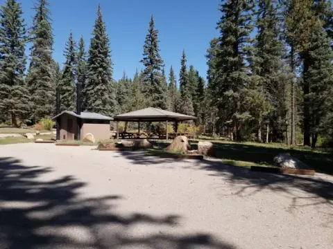 A parking area with a group shelter and vault toilet in a forest.