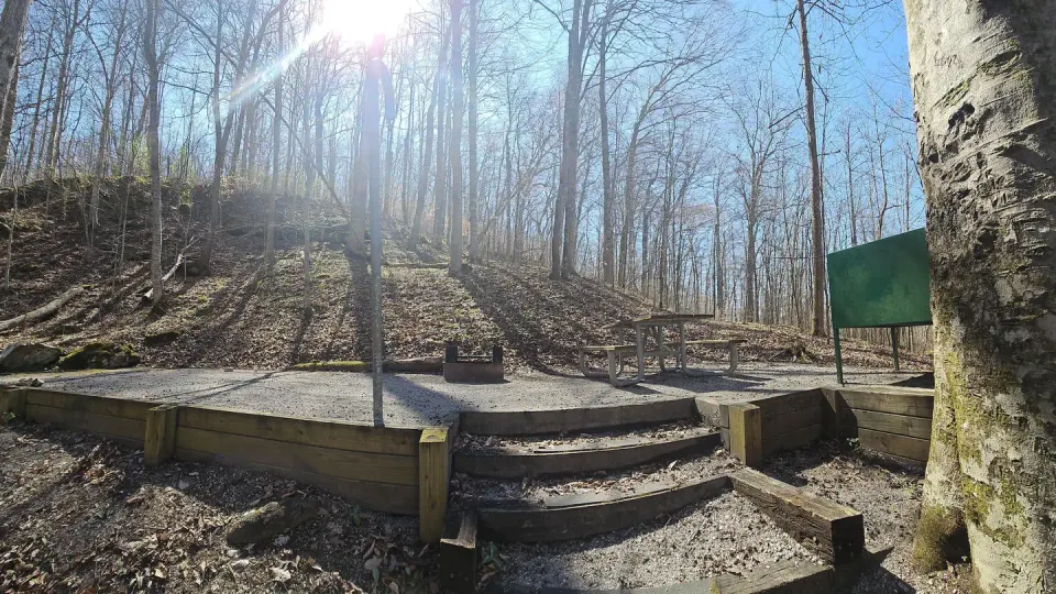 The sun shines down onto a gravel tent pad that has a picnic table and grill.