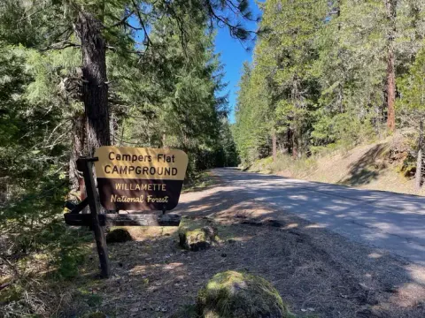 A brown and cream sign on a wooden stand. The sign reads "Campers Flat Campground".