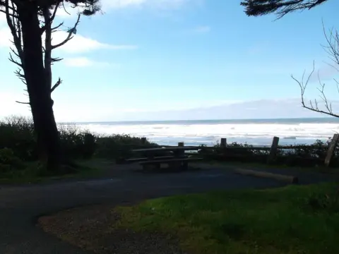 A campsite on a bluff overlooking the Pacific Ocean. The campsite has a paved parking spot as well as a picnic table and fire ring.