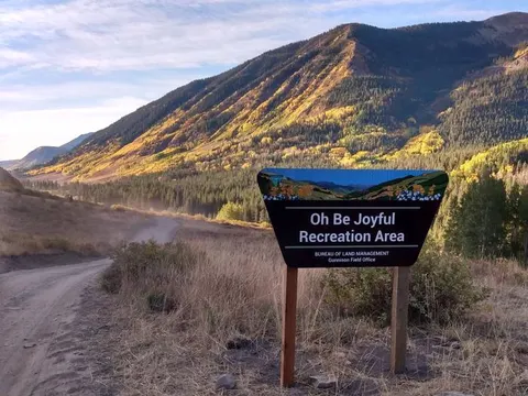 Oh Be Joyful Recreation Area Sign, entrance road, fall color mountains in the background