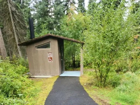 A photo of a Lake Alva Campground vault toilet. There is a paved, accessible walkway.