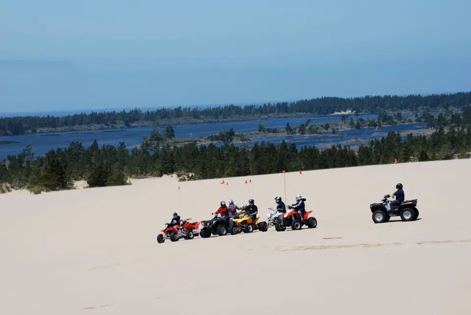 Off road vehicles on flat expanse of sand in front of blue lake ringed by conifer trees.