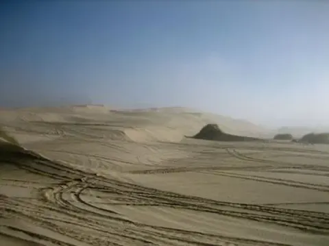 Sand dunes covered in OHV tracks, fog almost burned off.