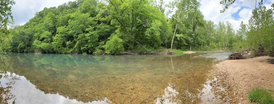 A view of Little Piney Creek, waterway in front with green vegatation in the background