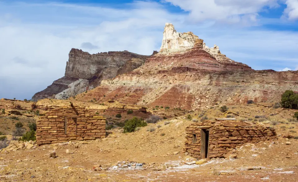 Stone cabin ruins with a sandstone butte in the background