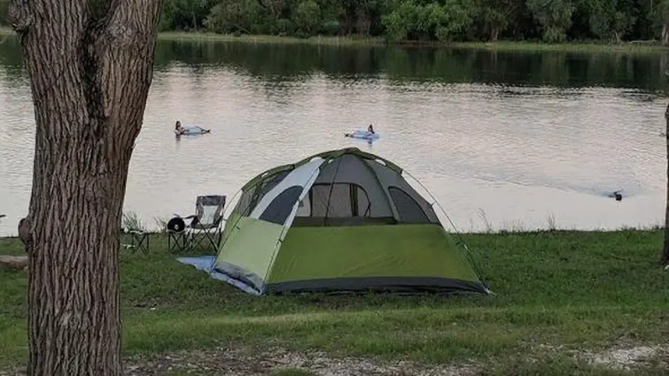 Green tent pitched on the shore of a lake.