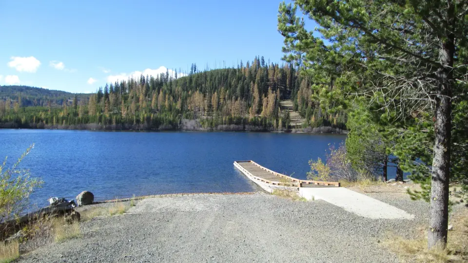 Olive Lake with water, boat dock and ramp, and conifers with fall color in the background.