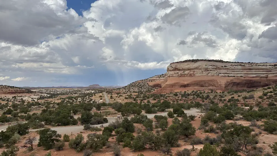An overview of Windwhistle Campground featuring individual campsites connected by a gravel road. All campsites have picnic tables and are near one of two vault toilets. Navajo sandstone cliffs rise to the south and east.
